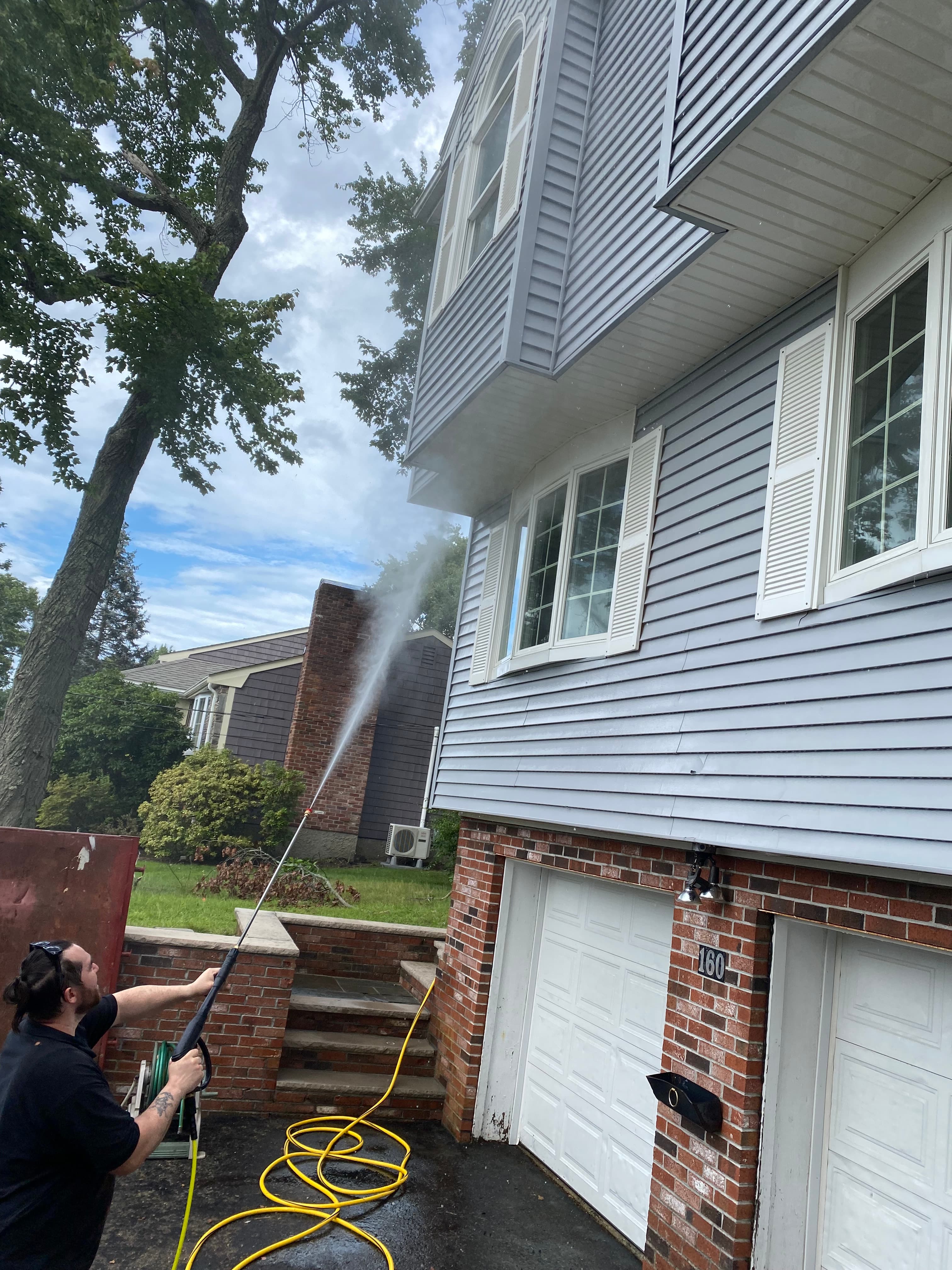 Man using a pressure washer to clean the light blue siding of a house.